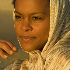 Gros plan d'une femme avec un foulard beige tissé sur la tête, le regard tourné sur le côté, dans la lumière dorée du coucher de soleil