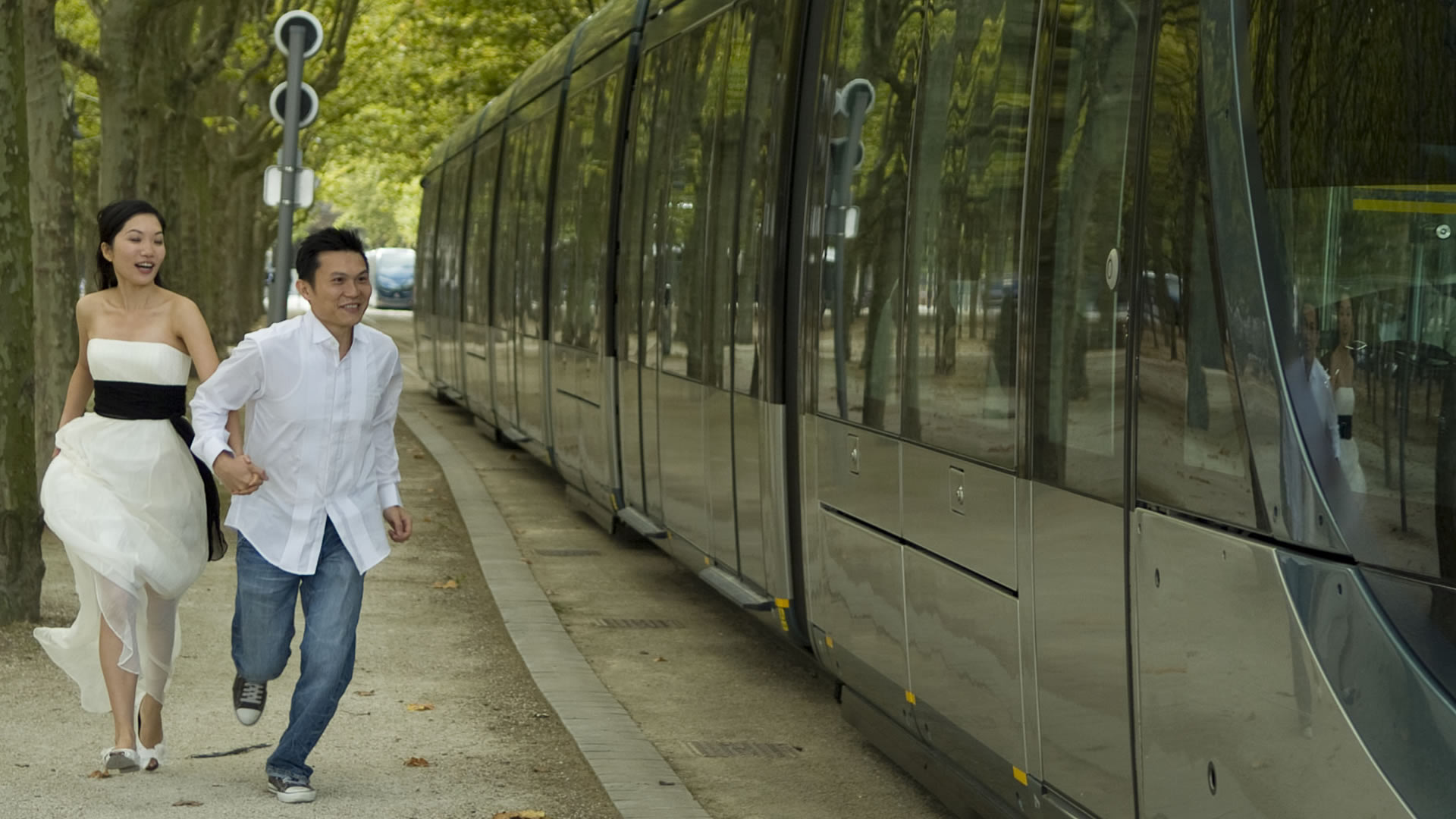 Couple courant main dans la main sur un chemin bordé d'arbres, le long d'un tramway moderne à Bordeaux