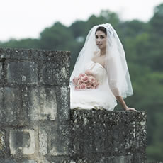 Portrait de mariage artistique d'une mariée en robe blanche et voile, tenant un bouquet de roses roses près d'un vieux mur de pierre