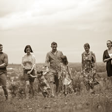 Portrait de famille aux tons sépia d'adultes et d'enfants marchant ensemble dans une prairie de fleurs sauvages.