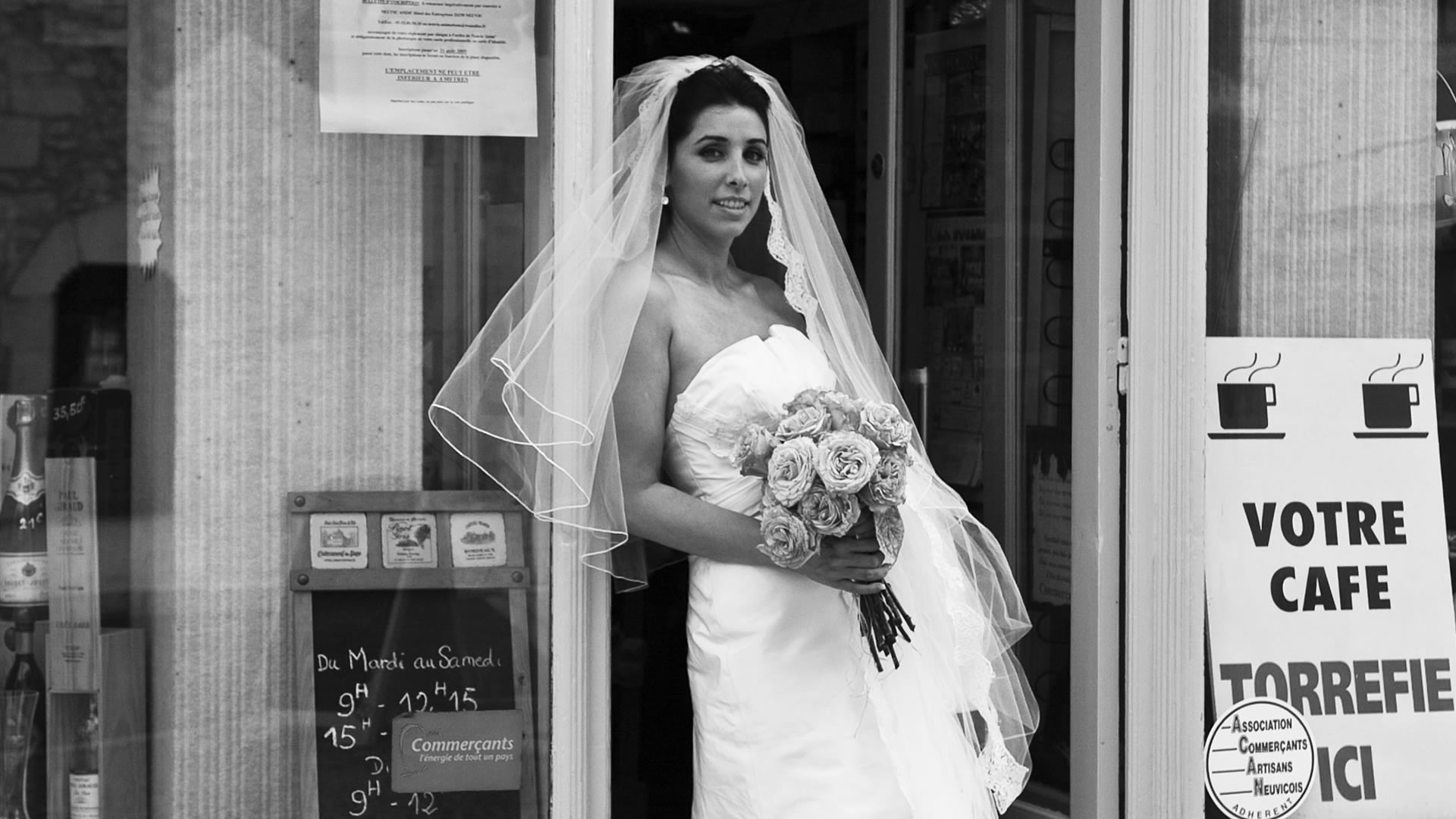 Photographie de mariage en noir et blanc d'une mariée tenant son bouquet devant un café français traditionnel