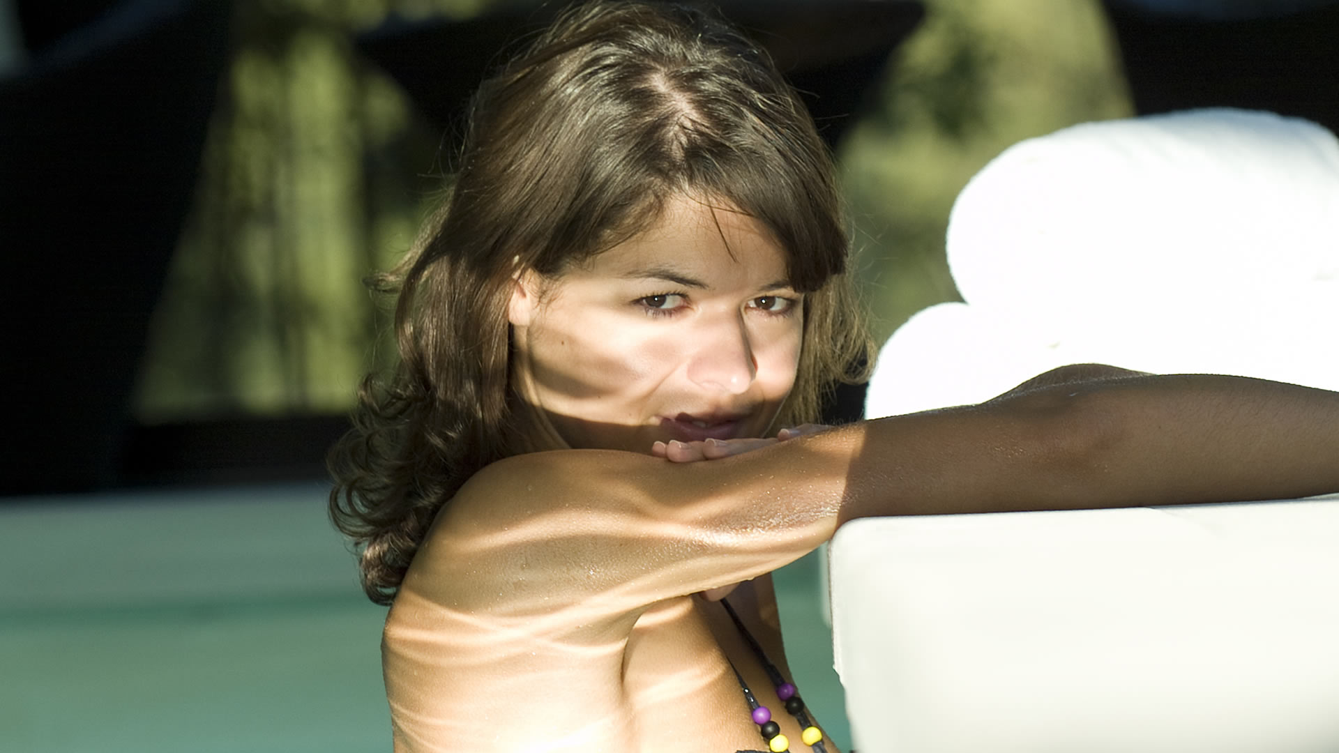 Femme aux cheveux bruns ondulés, le menton posé sur son bras, regardant l'objectif, avec des taches de lumière sur les épaules